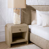 A bedroom vignette featuring the Eichholtz Nightstand ArtDeco — geometric brass inlay, warm tones, and a sculpted base beside a styled upholstered bed.