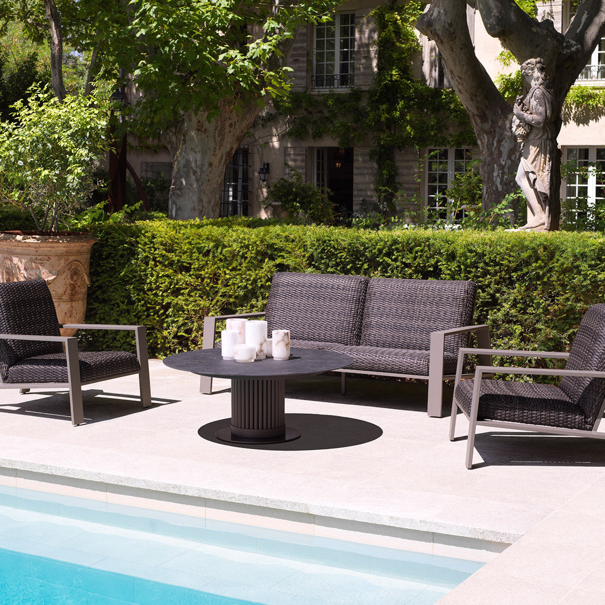 Eichholtz Outdoor Sofa Belle Vue paired with two lounge chairs and a round coffee table by a pool — the sofa-first vignette laid out exactly the way the showroom recommends planning a patio.
