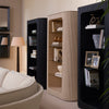 Two Bogota display cabinets in charcoal oak veneer styled in a luxury living room with books, brass accessories, a floor lamp, and a curved white sofa