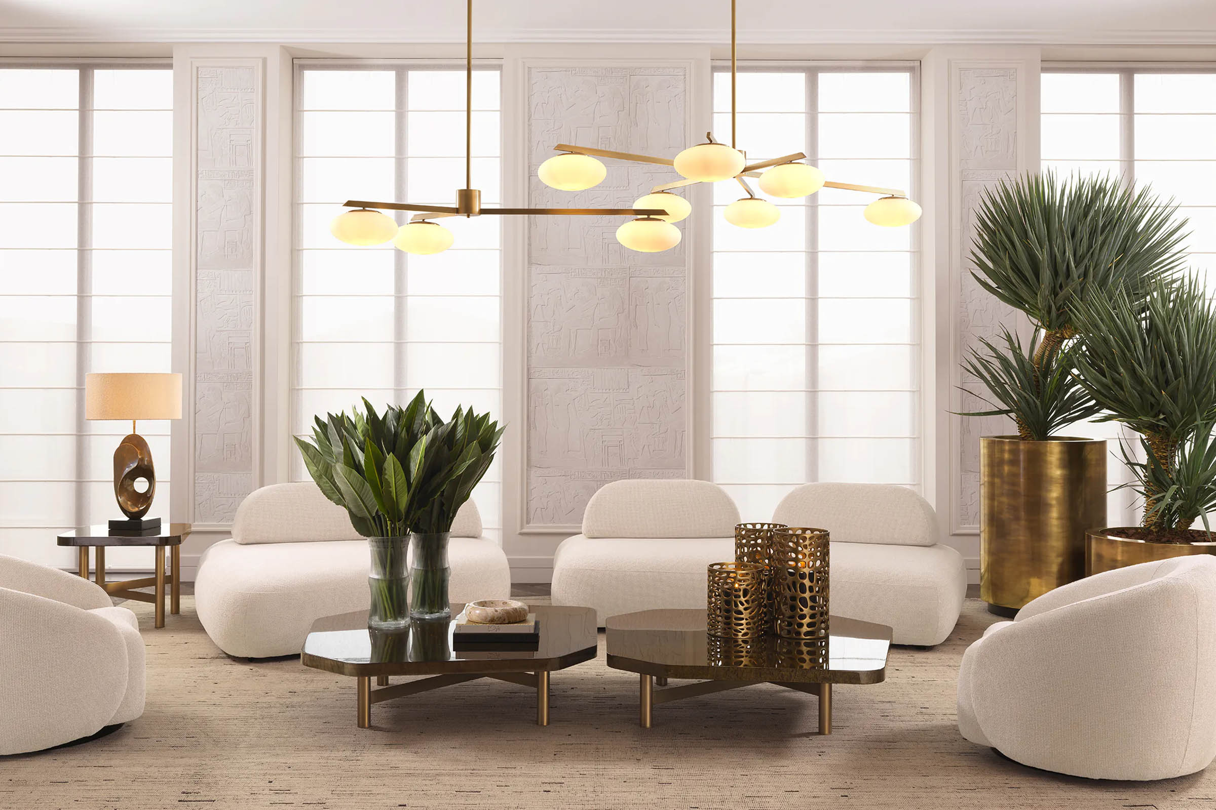 A curated Eichholtz living-room vignette — cream boucle seating, brass chandelier, layered stone-and-brass coffee tables — the kind of in-stock luxury that ships fast and furnishes a room on schedule.