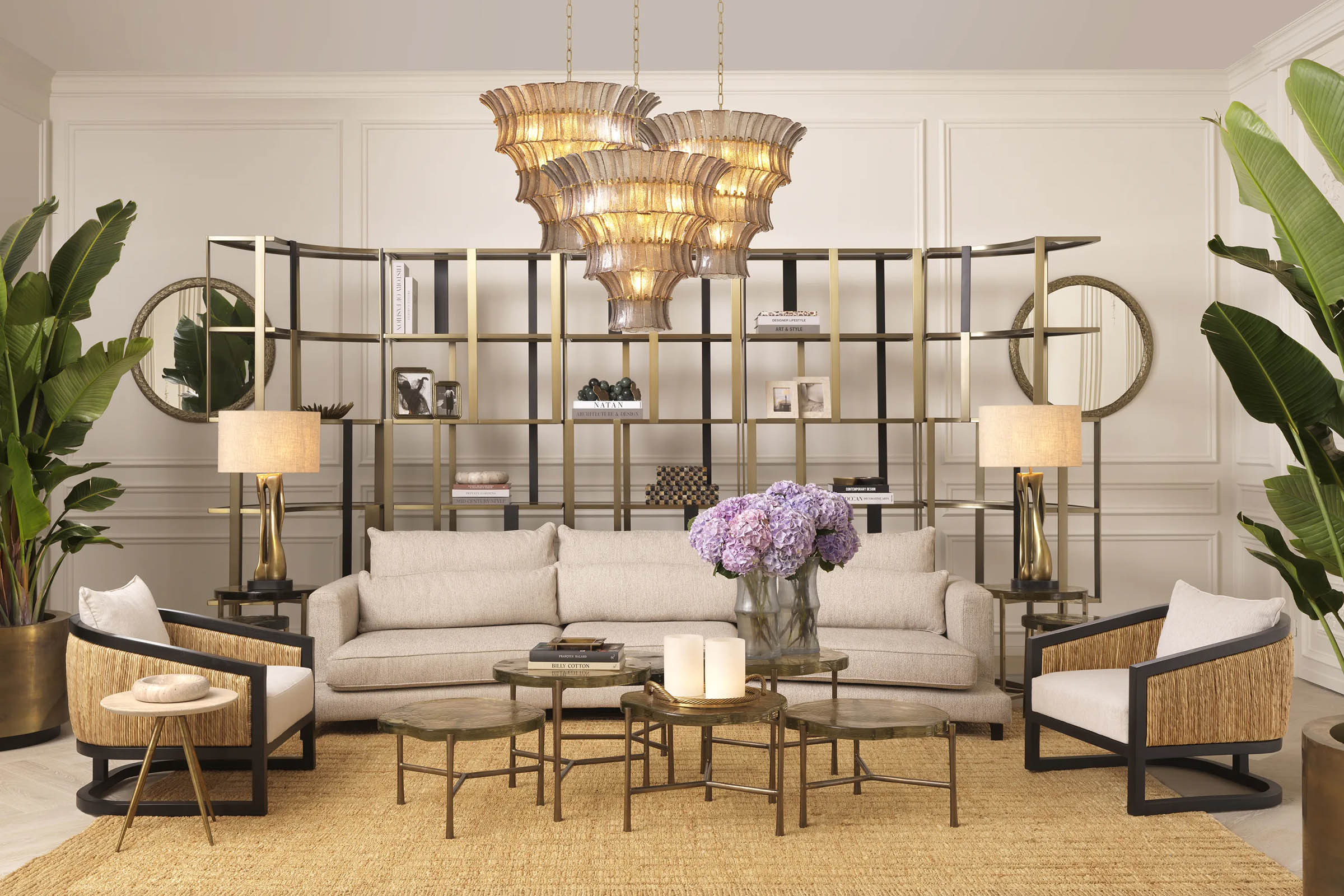 A curated Eichholtz living-room vignette — cream sofa, brass étagère, tiered chandelier — the kind of specification work the Designer Trade Program supports.