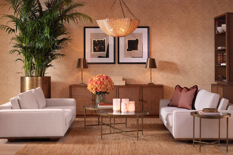 A warm living room with a rattan sideboard flanked by brass table lamps and wall art, cream sofas, and a wicker chandelier — the sideboard as a defining piece in a composed interior