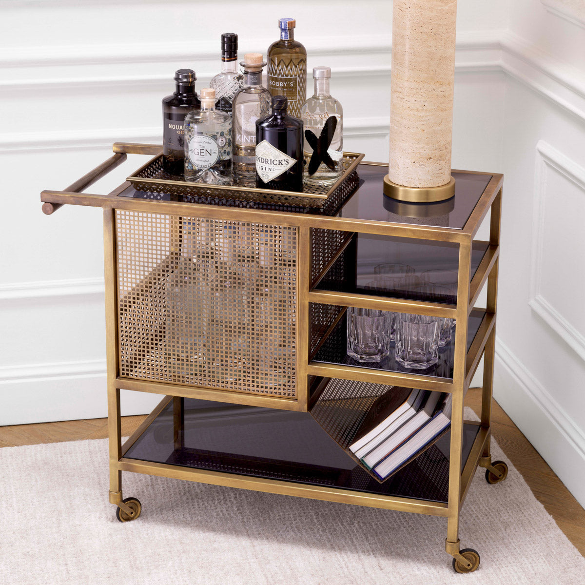 Trolley Sterling styled as a drinks station — brass frame, black glass shelves with bottles and decanters, white paneled walls