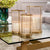 Eichholtz lanterns and candleholders in polished metal and glass casting a warm glow in a modern luxury interior.