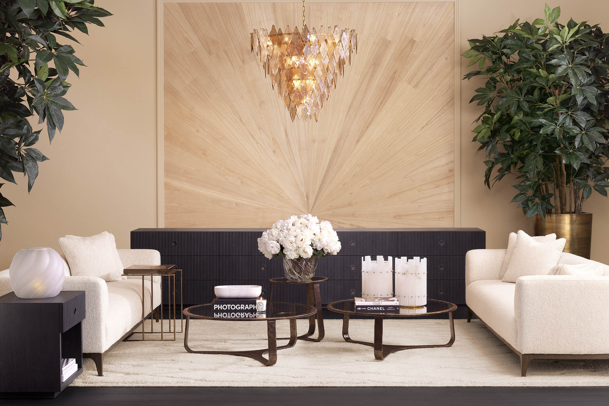 A curated Eichholtz living-room vignette — dark fluted credenza against a light wood feature wall, cream sofas, amber geometric chandelier