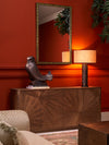 Wooden cabinet with geometric veneer styled with sculptural bird décor, table lamp, and framed wall mirror against deep red walls in an elegant interior.