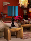 Luxury living room vignette with gold textured side table, sculptural table lamp with blue shade, red floral arrangement, plush seating, and deep red paneled walls.