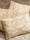 Close up of cream textured decorative pillows with abstract woven pattern resting on a neutral upholstered surface.