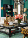 Elegant living room with emerald green walls, patterned accent pillows, black studded coffee table, floral arrangement, sculptural lighting, and layered luxury décor.