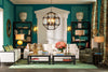 Luxury living room with deep teal paneled walls, ivory upholstered seating, warm metallic lighting, dark shelving, and curated décor reflecting refined European interior design.