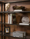 Open shelving unit styled with books, sculptural décor, framed photograph, and geometric storage box against warm wood paneling.