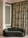 Curved green velvet sofa positioned beneath patterned drapery and decorative wall moldings in a refined living space.