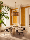 Luxury dining area with round table, upholstered dining chairs, sculptural chandelier, classical columns, and golden walls bathed in natural light.