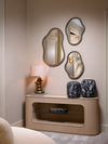 Curved wood console table with sculptural mirrors, decorative vases, and table lamp styled against soft neutral walls in a refined interior.