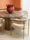 Round stone dining table with upholstered dining chairs and brass legs styled in a warm, elegant dining space.