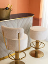 Luxury bar setting with upholstered bar stools, sculptural curved bar front, brass bases, and warm neutral tones in an elegant interior.
