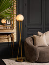 Brass floor lamp with glowing glass globe positioned beside a curved upholstered chair against dark paneled walls and a decorative mirror.